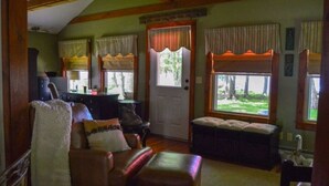 A cozy living room with a fireplace, leather sofa, and a view of the outdoors through large windows. - Charming cottage on the water with beautiful views (Lakeville)