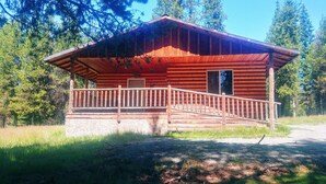 Une cabane en bois dotée d’un porche et d’une porte, entourée d’arbres.