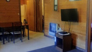 Une pièce avec un intérieur en bois, une table à manger avec des chaises, un téléviseur posé sur un meuble et une horloge au mur.