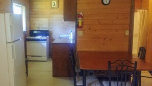 Une cuisine compacte équipée d’un réfrigérateur, d’une cuisinière et d’un évier. On y trouve une table à manger avec des chaises et une horloge au mur.