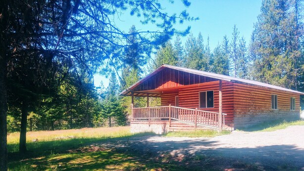 Un chalet rustique doté d’un porche en bois et d’un espace abrité, entouré d’un paysage boisé.