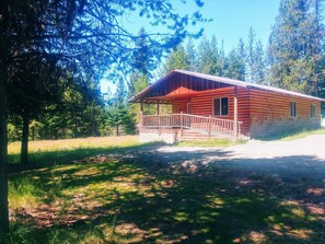 A rustic cabin with a wooden porch and a covered area, surrounded by a forested landscape. -  Bear Cabin (Elk City)