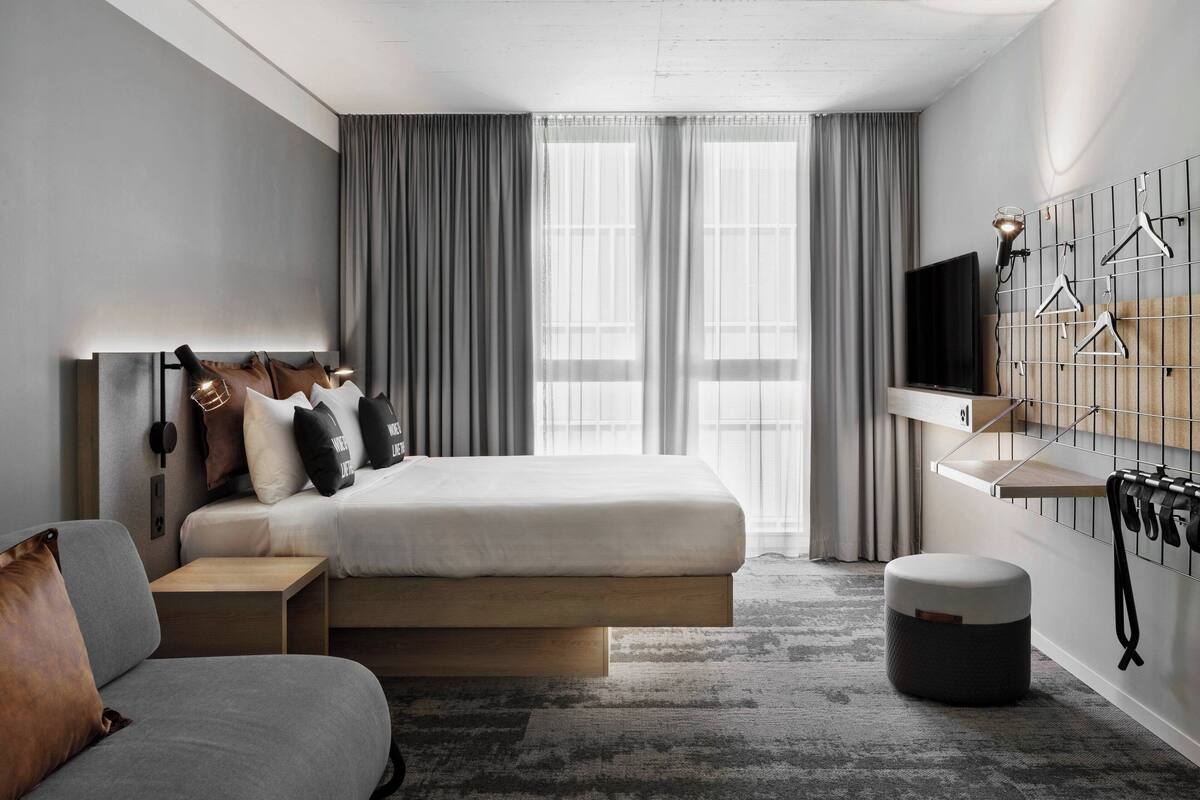 Una habitación de hotel moderna con cama, sofá, una mesita, televisor y perchero en la pared.