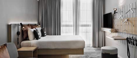 Una habitación de hotel moderna con cama, sofá, una mesita, televisor y perchero en la pared.