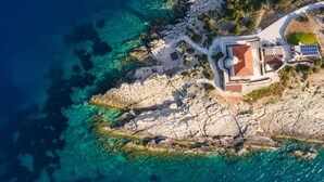 An aerial view of a coastal property with a central building, a paved pathway, and a rocky shoreline. - Luxury Villa Lighthouse Beyond (Vis)
