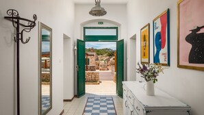 A hallway with a checkered floor, a coat rack, a mirror, a green door leading outside, and a white dresser with a vase of flowers. - Luxury Villa Lighthouse Beyond (Vis)