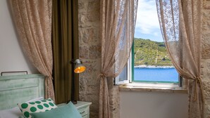 A bedroom with a bed, a nightstand, a lamp, and a window with curtains. - Luxury Villa Lighthouse Beyond (Vis)