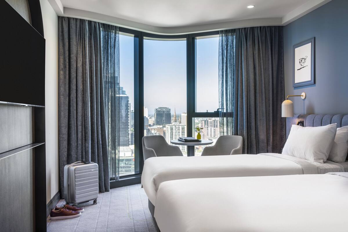 A hotel room with two beds, a desk, and a view of the city.