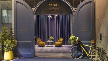 A hotel entrance with a dark blue curtain, two yellow armchairs, a small table with a vase, and a bicycle.