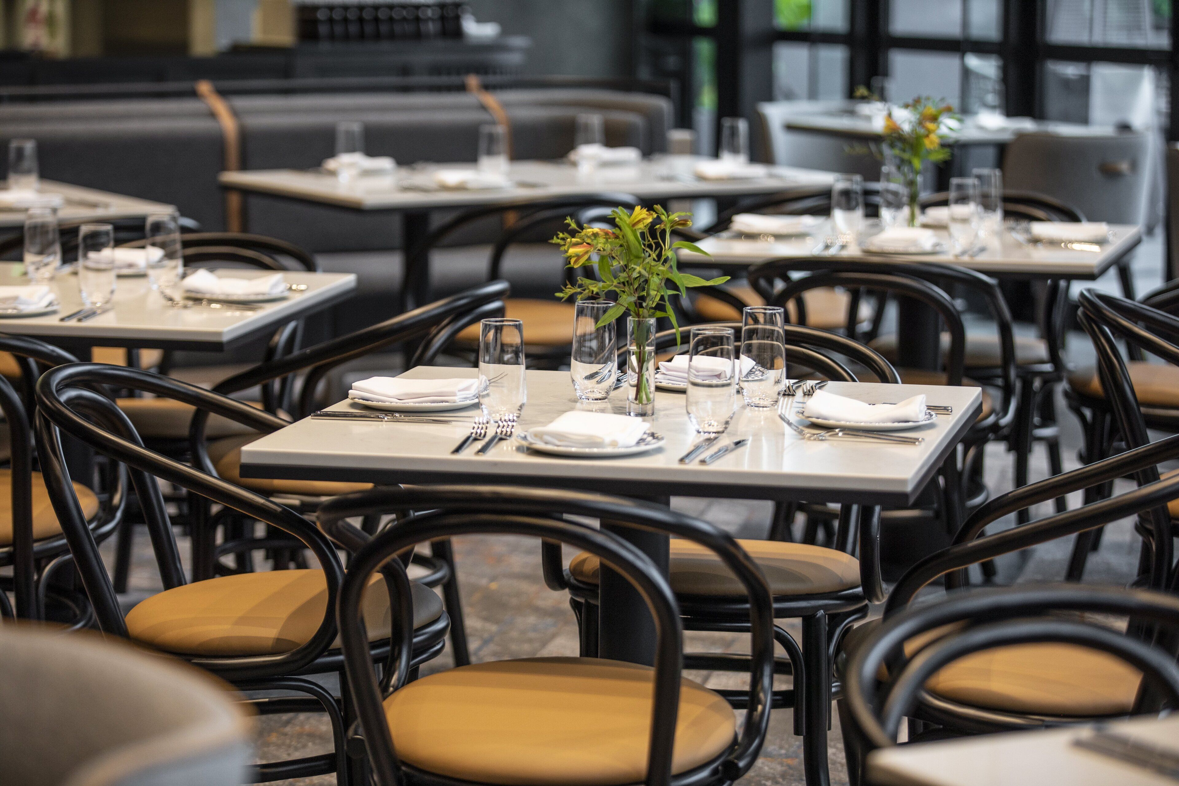 Un restaurante con mesas dispuestas para comer, sillas y un jarrón con flores.