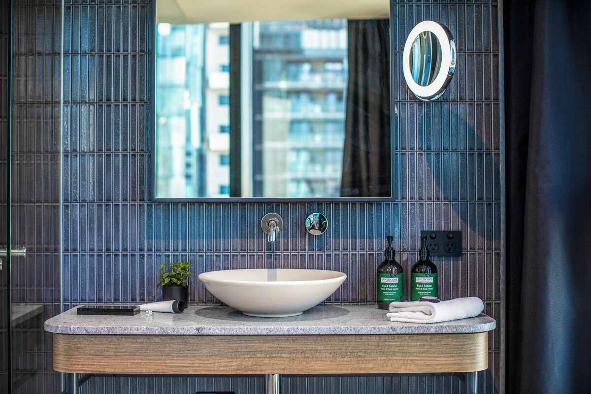 Un baño moderno con un lavamanos grande, un espejo y vistas a edificios altos.