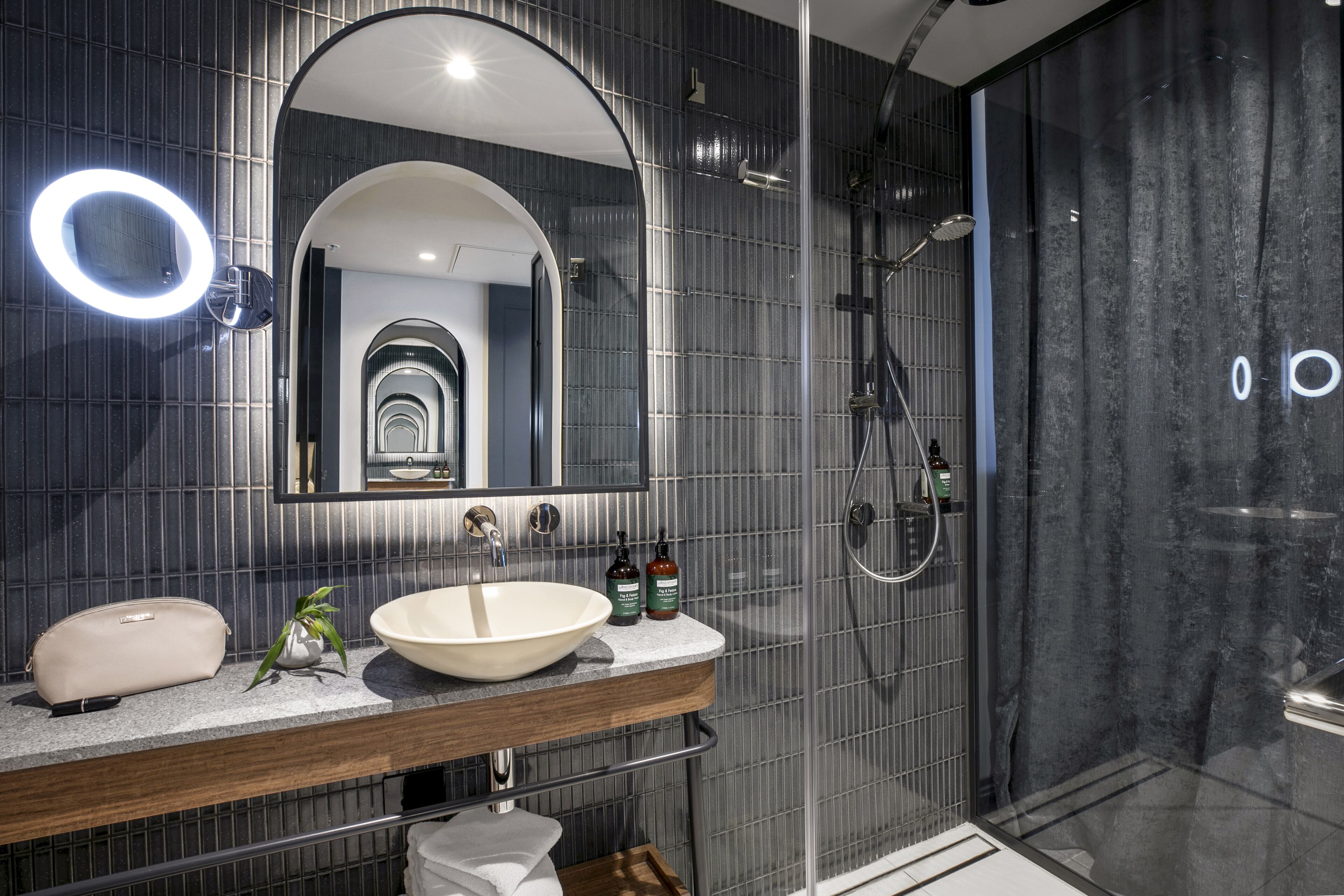 A modern bathroom with a large mirror, a round light, a sink, and a shower.