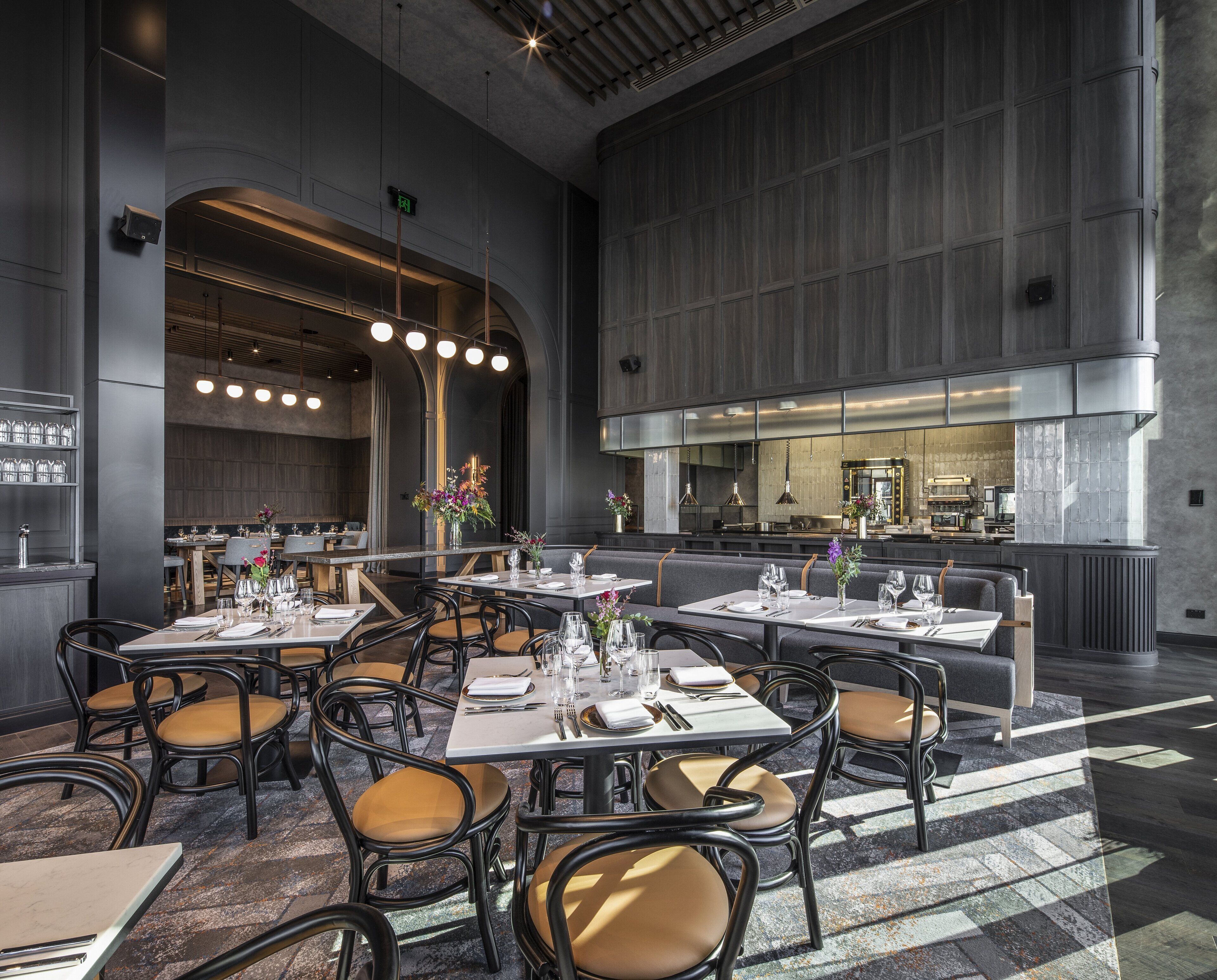En rummelig restaurant med højt til loftet, moderne belysning og et centralt køkkenområde.