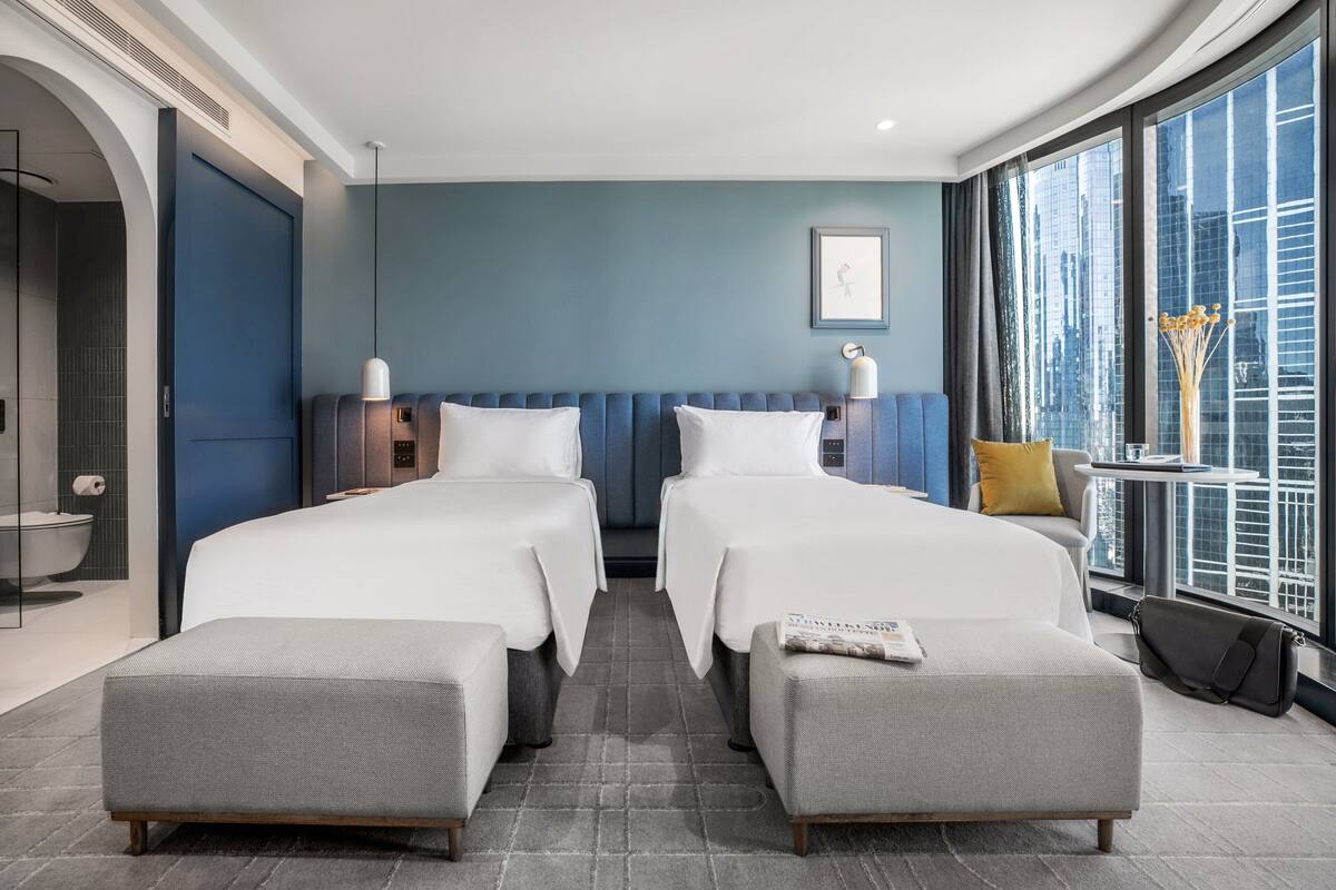 A hotel room with two beds, a sofa, a small table, and a window with a city view.