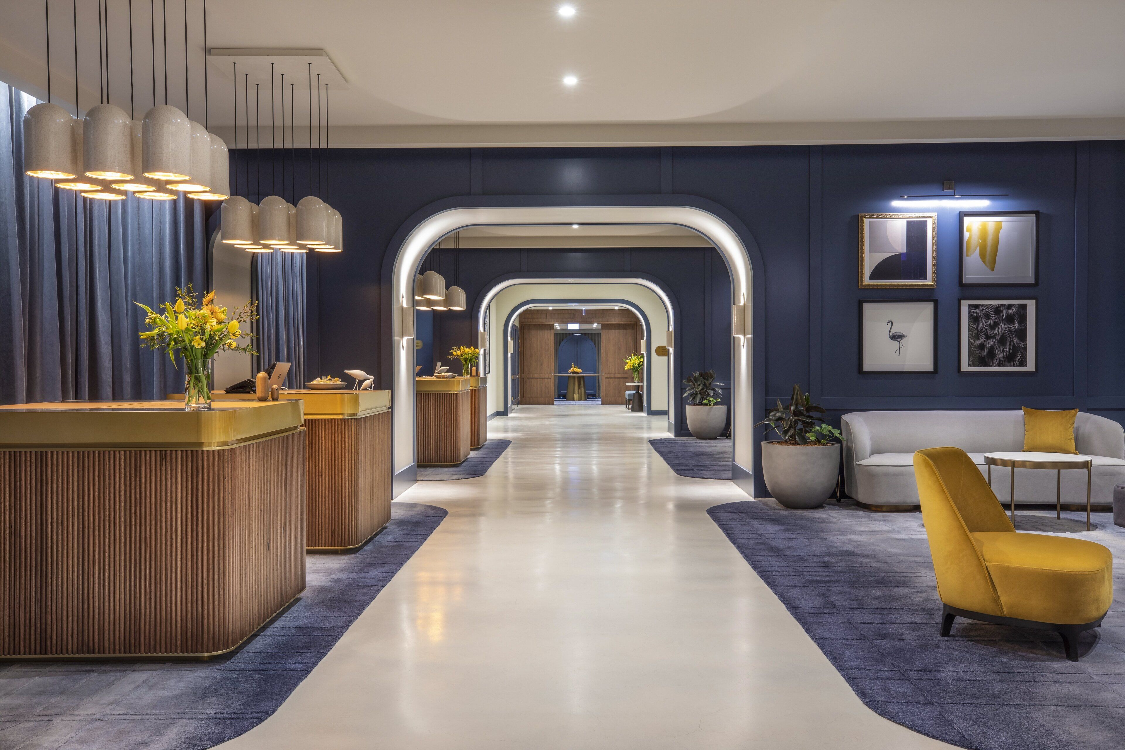 A modern lobby with a reception desk, seating area, and a hallway leading to a room.