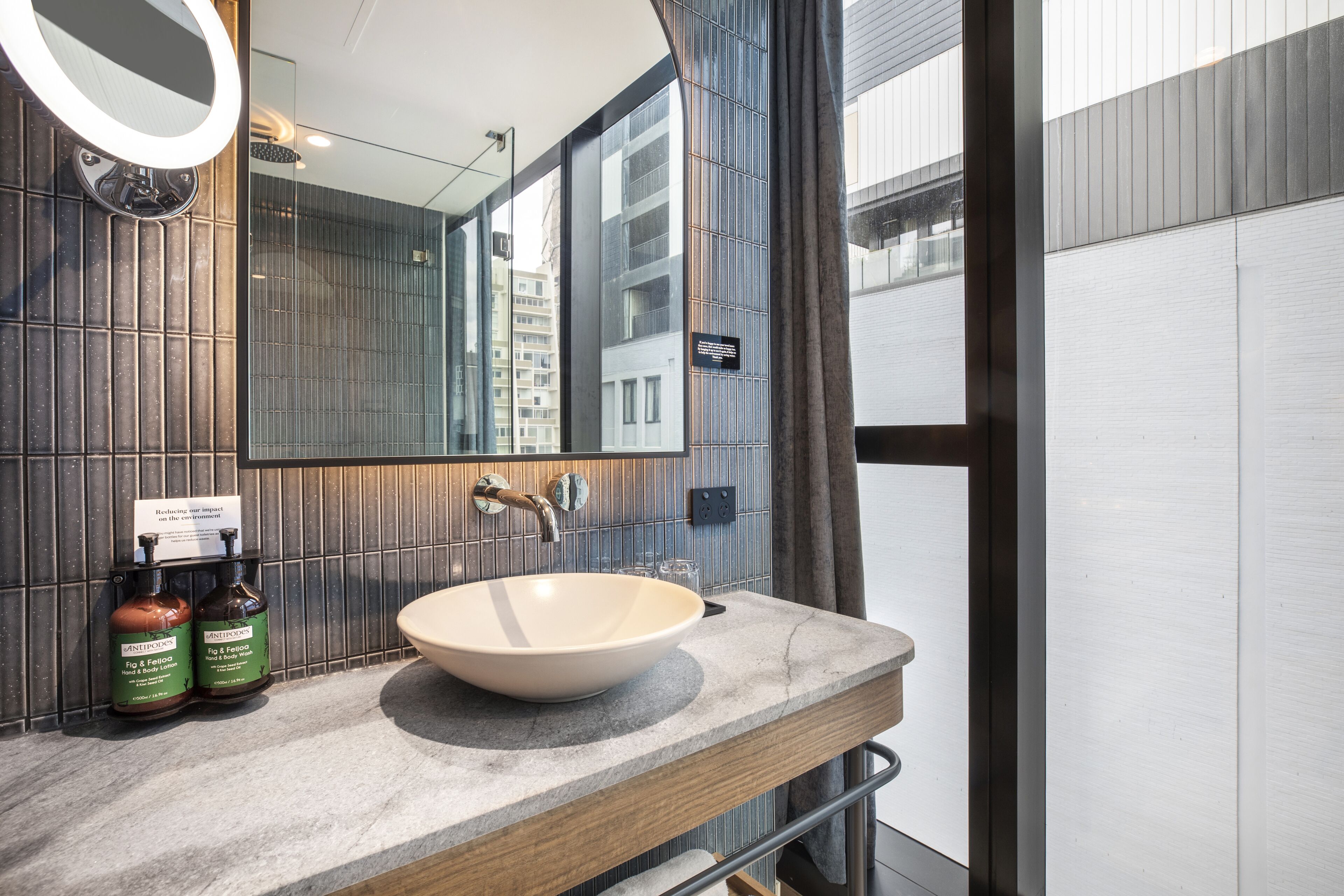 A modern bathroom with a large mirror, a beige sink, and two bottles of shampoo.
