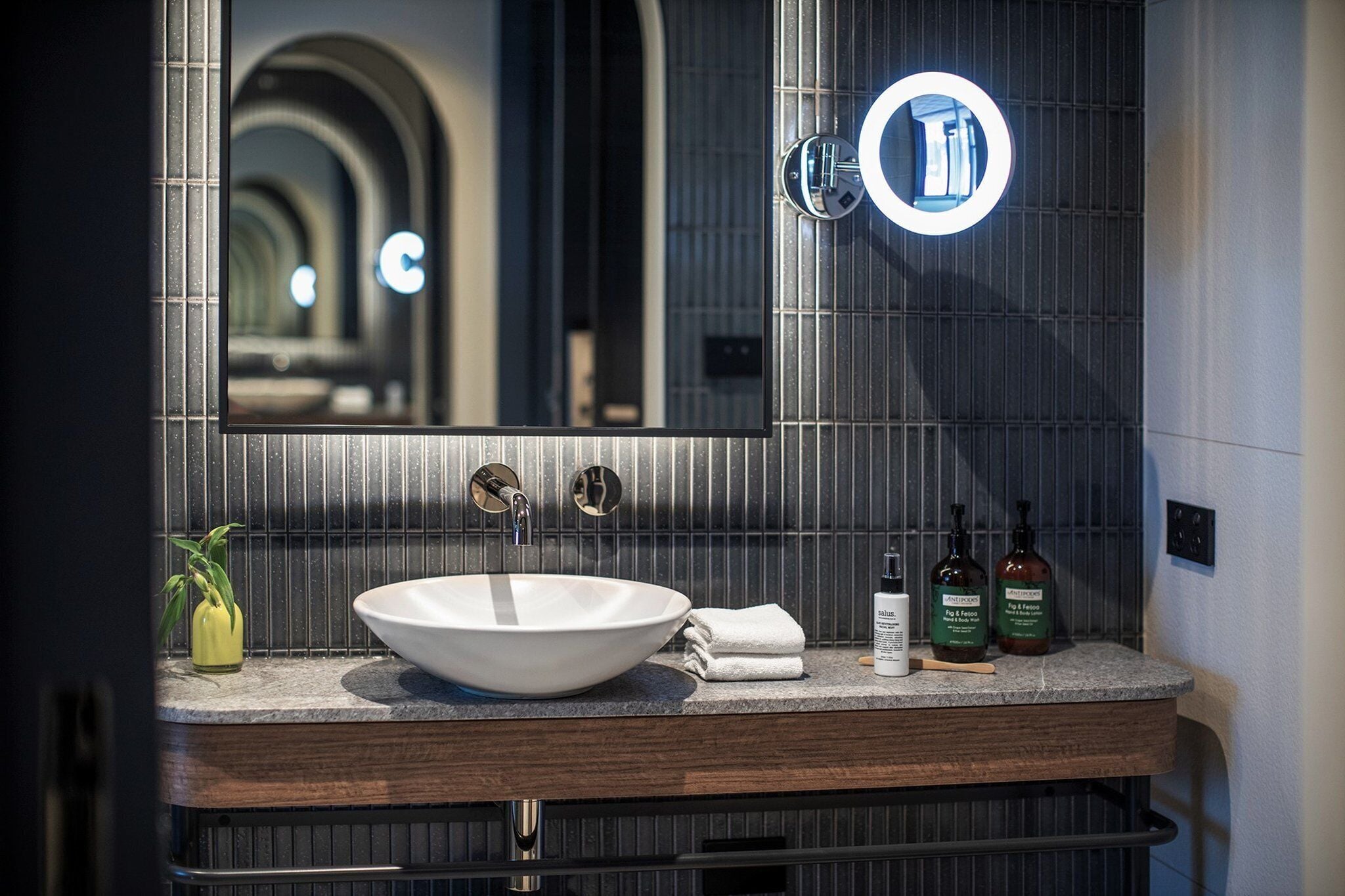 Un baño moderno con un espejo grande, un lavabo sobre encimera y un mueble de tocador con artículos de aseo.