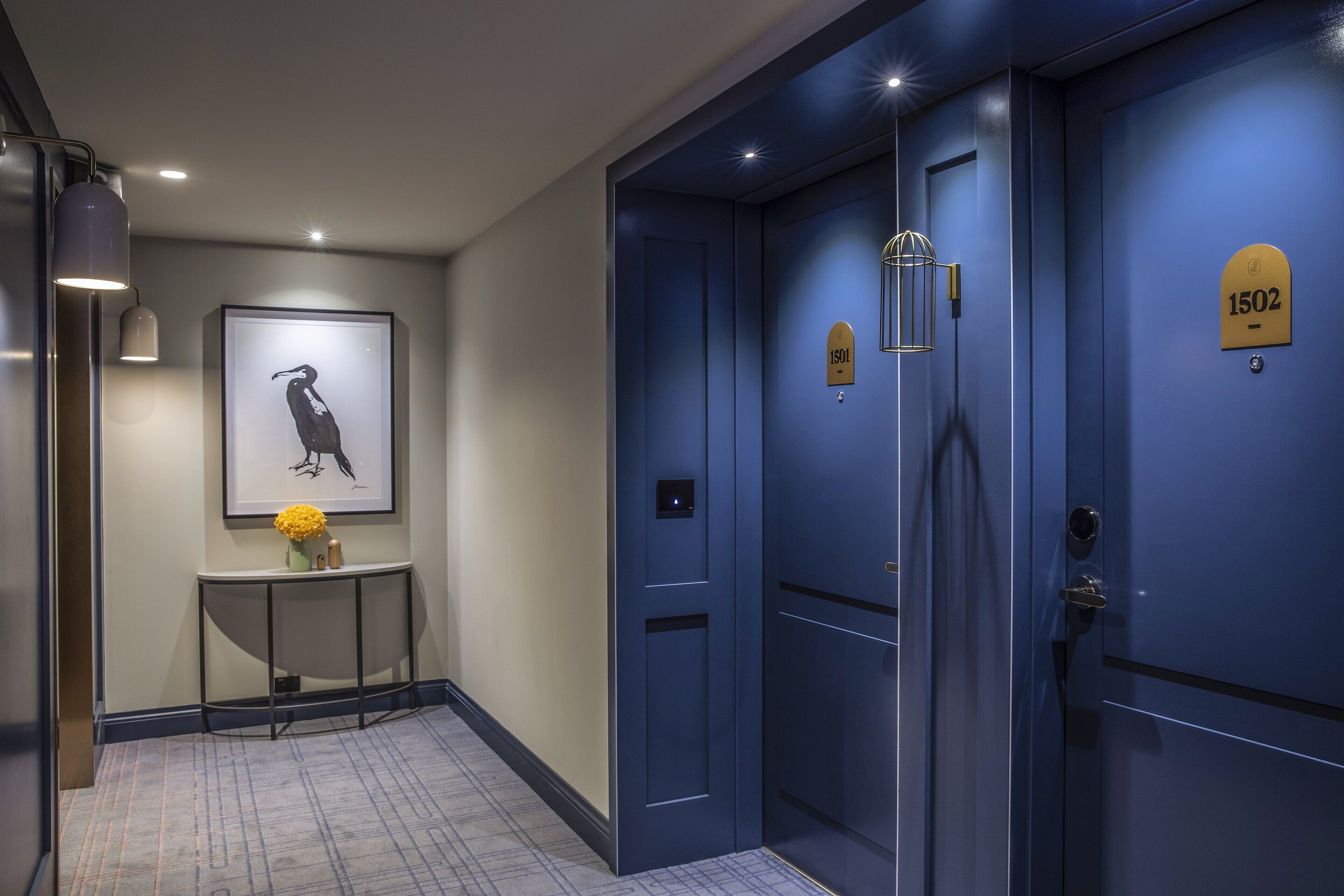 A modern hallway with a blue door marked "1502," a framed artwork on the wall, and a console table with a vase.
