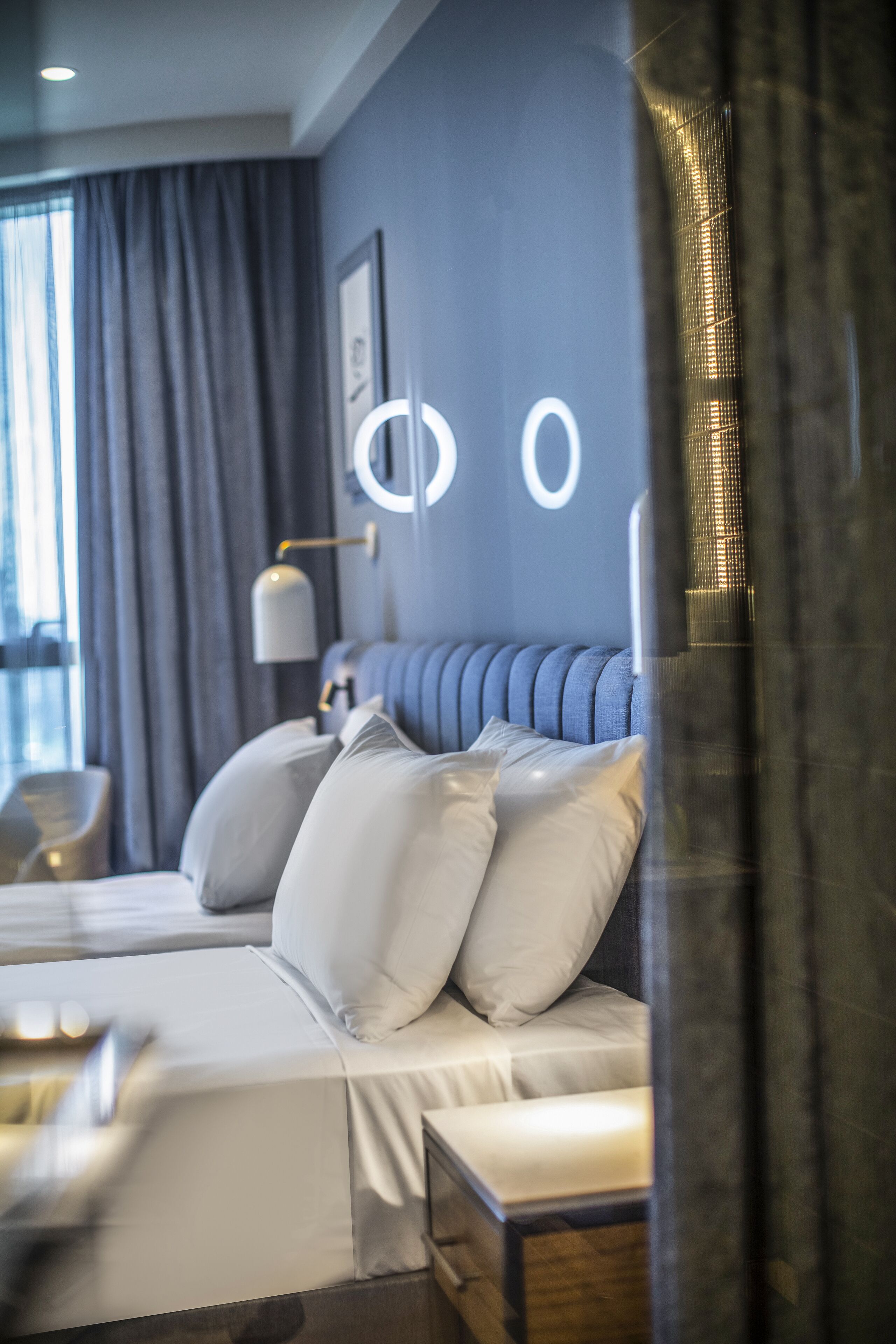 Una habitación de hotel moderna con una cama grande, una mesita de noche, una lámpara y vistas a un edificio.