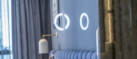 Una habitación de hotel moderna con una cama grande, una mesita de noche, una lámpara y vistas a un edificio.