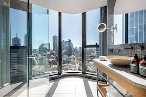 A modern bathroom with a large window, a round mirror, and a sink with toiletries. - voco Melbourne Central by IHG (Melbourne)