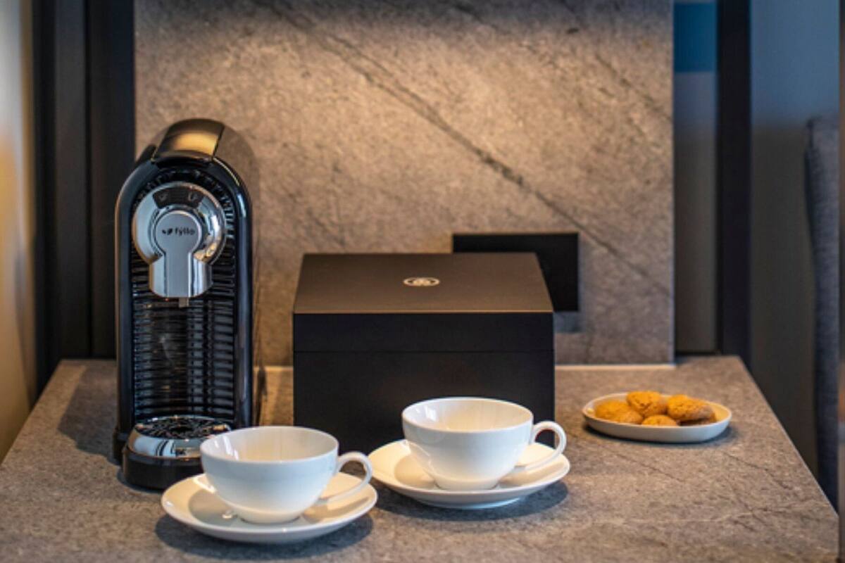 A coffee machine, two white cups, and a box on a marble countertop.