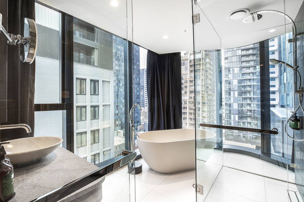 A modern bathroom with a freestanding bathtub, a double sink, and a large window offering a city view.