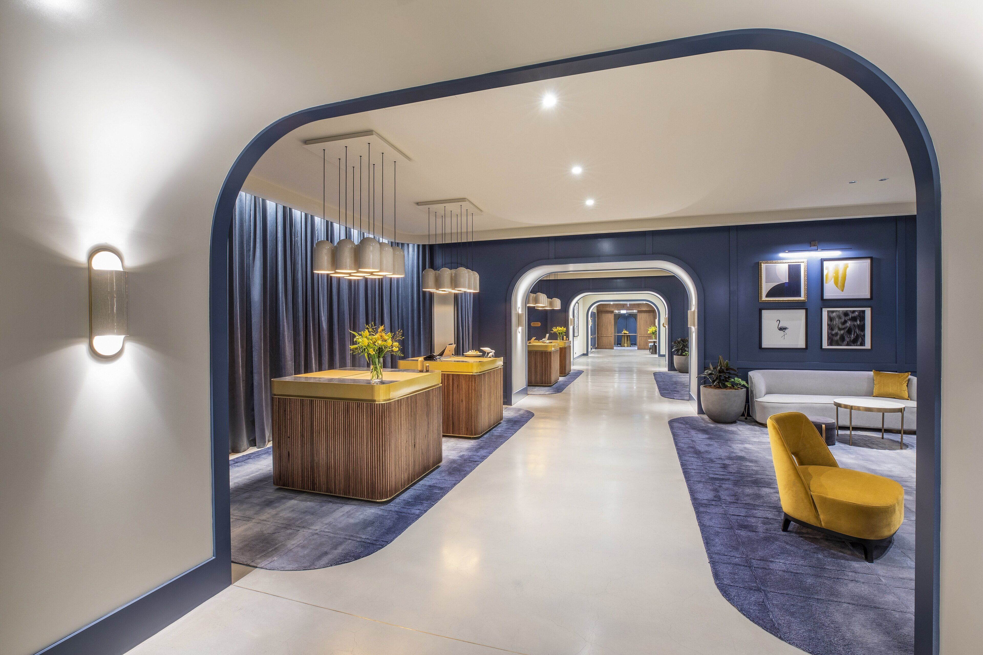 A modern hotel lobby with a reception desk, seating area, and a view into the rooms.