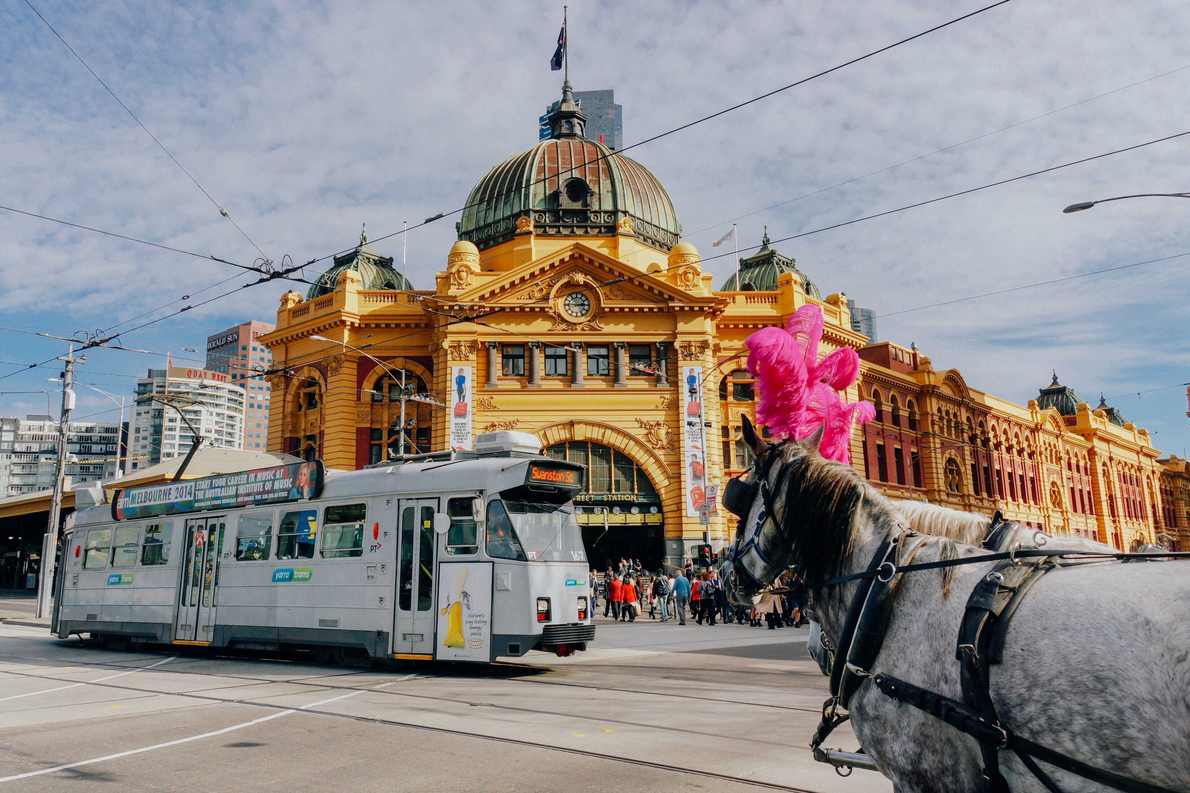 A tram and a horse-drawn carriage in front of a historic building with a large dome and arched windows.