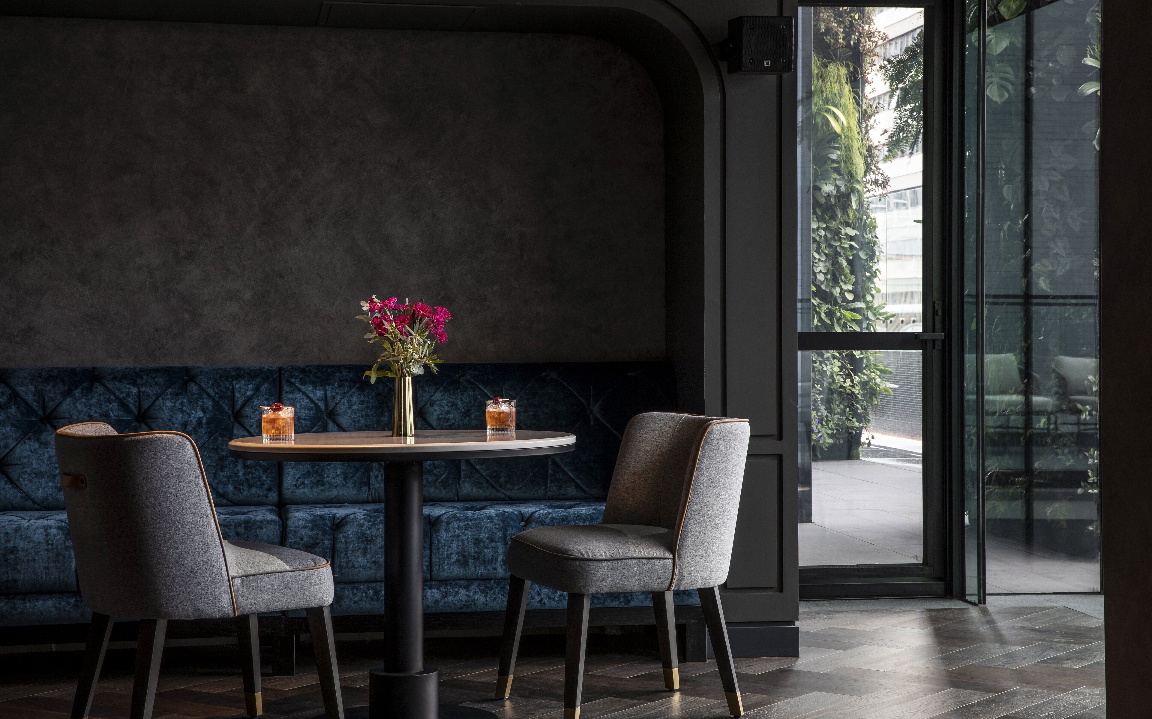 A modern interior with a round table, two chairs, a vase with flowers, and a view through a large window.