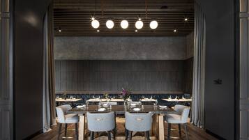 A modern dining area with a central island, round tables, and grey upholstered chairs.