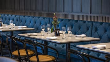 Un restaurante con cabinas tapizadas en azul, mesas de madera y sillas con cojines amarillos.