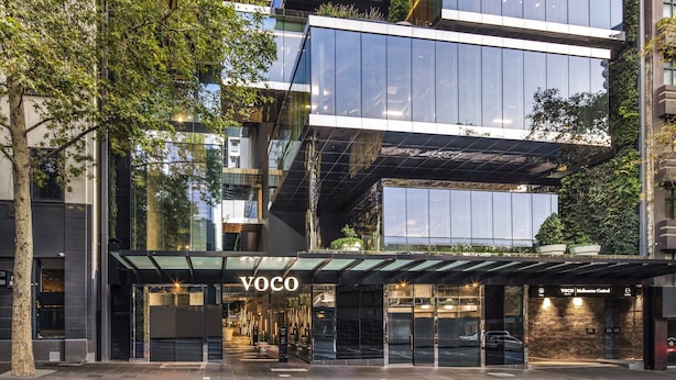Un edificio moderno con fachada de vidrio, un área de entrada techada y el nombre "Voco" bien visible.