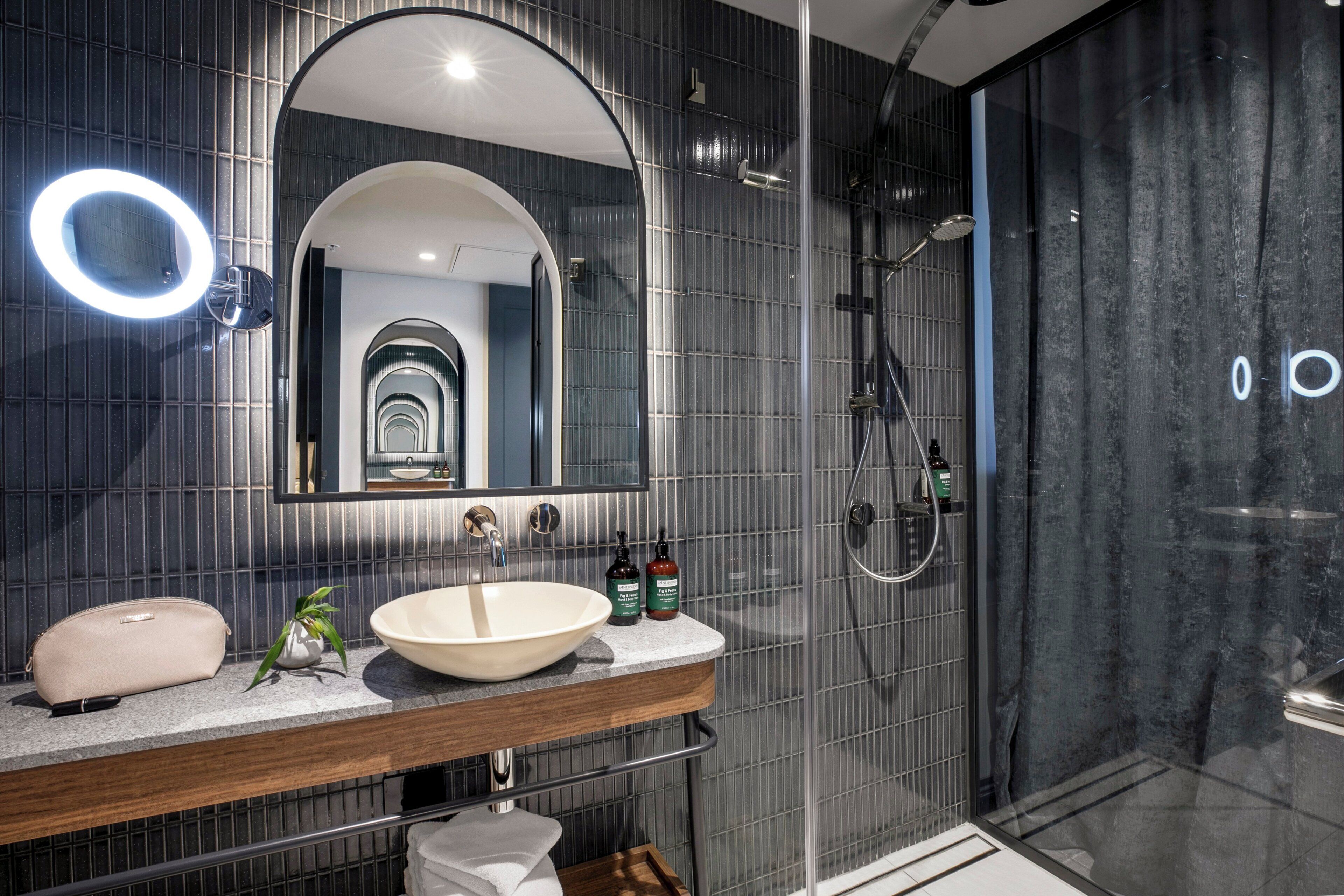 Un baño moderno con un espejo grande, una lámpara redonda, un lavamanos y una zona de ducha.