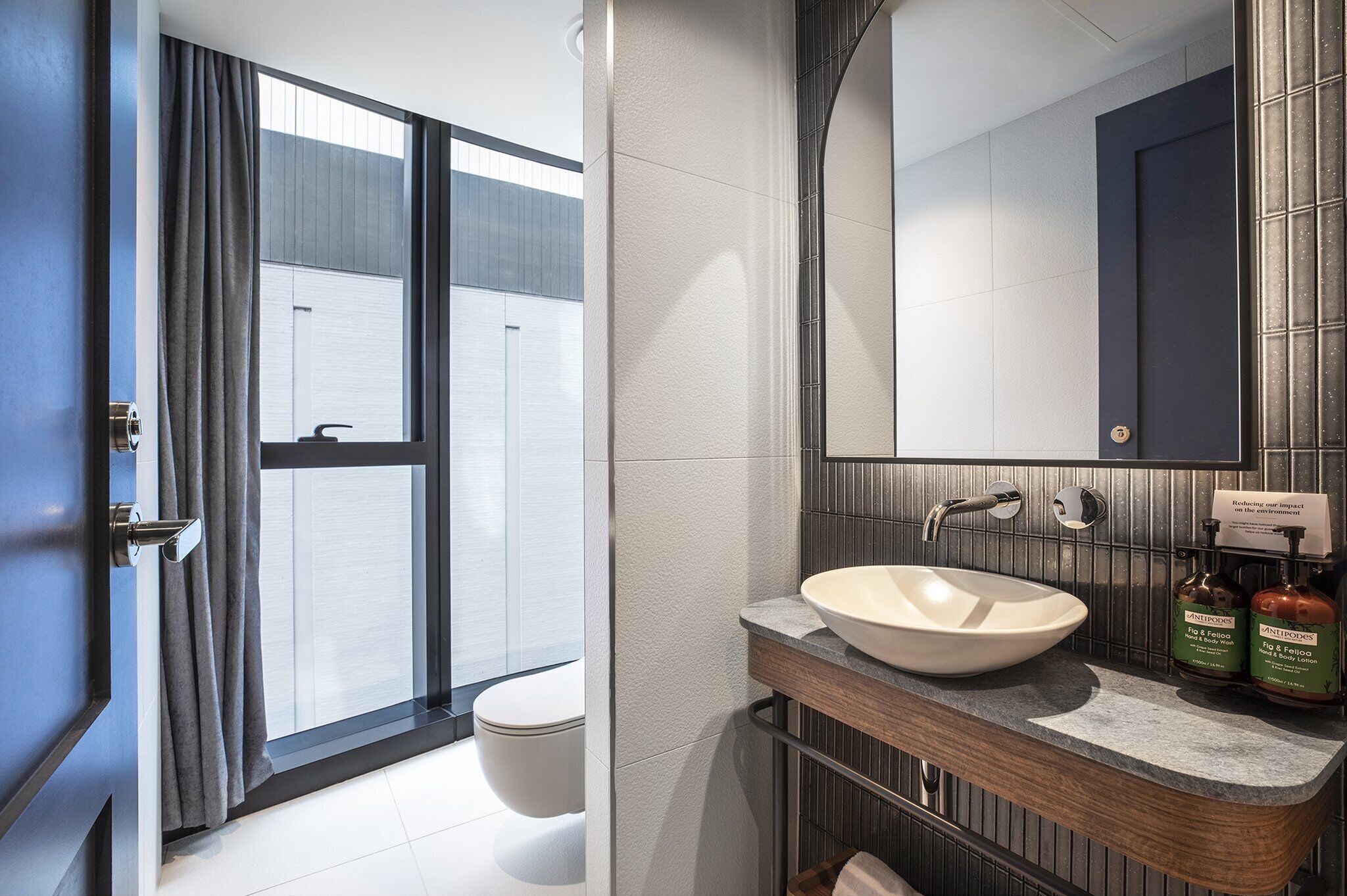 A modern bathroom with a large window, a white sink, and a mirror above it.