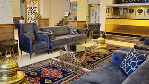 Un moderno vestíbulo de hotel con un mostrador de recepción, una zona de estar y elementos decorativos como un candelabro y alfombras estampadas.