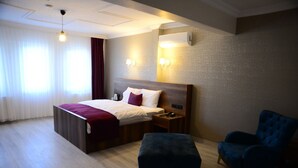 Una habitación de hotel con cama, mesita de noche, lámpara y un sillón azul.