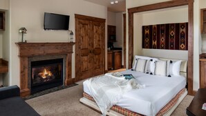 A bedroom with a fireplace, a bed with white bedding, a television, and a patterned wall hanging.