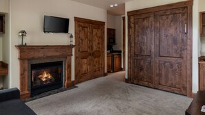 A living room with a fireplace, a television mounted on the wall, and wooden doors.