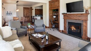 A living room with a fireplace, a television mounted above it, and a dining area in the background.