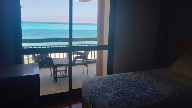 Una habitación con cama, escritorio y vista al océano a través de un gran ventanal.