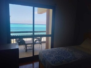 Una habitación con cama, escritorio y vista al océano a través de un gran ventanal.