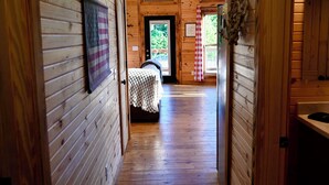 A wooden cabin interior with a hallway leading to a bedroom.
