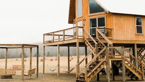 A wooden cabin with a large window, a balcony, and a staircase leading to the main floor.