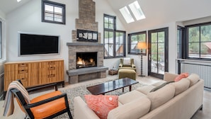 A spacious living room with a stone fireplace, a flat-screen TV, a sofa, and a coffee table. - 211 South Oak Street C | Luxury Telluride Townhome Steps to the Gondola (Telluride)