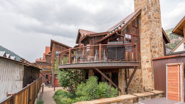 A rustic cabin with a stone chimney, wooden balconies, and a covered outdoor seating area. - 211 South Oak Street C | Luxury Telluride Townhome Steps to the Gondola (Telluride)