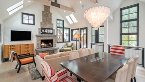 A spacious living room with a large wooden dining table, comfortable seating, a fireplace, and a television mounted on the wall. - 211 South Oak Street C | Luxury Telluride Townhome Steps to the Gondola (Telluride)