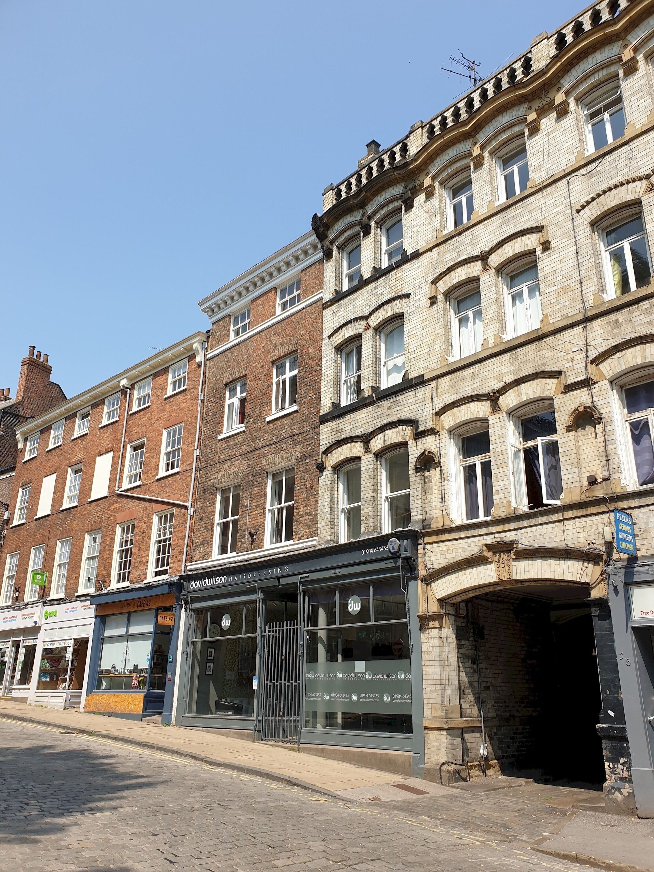 A street view with a row of multi-story buildings, including a hairdressing salon and a pizza restaurant.
