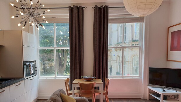 A modern living room with a sofa, a dining table, and a TV. - St Martins View - Two Bedroom Apartment, Sleeps 4 (York)