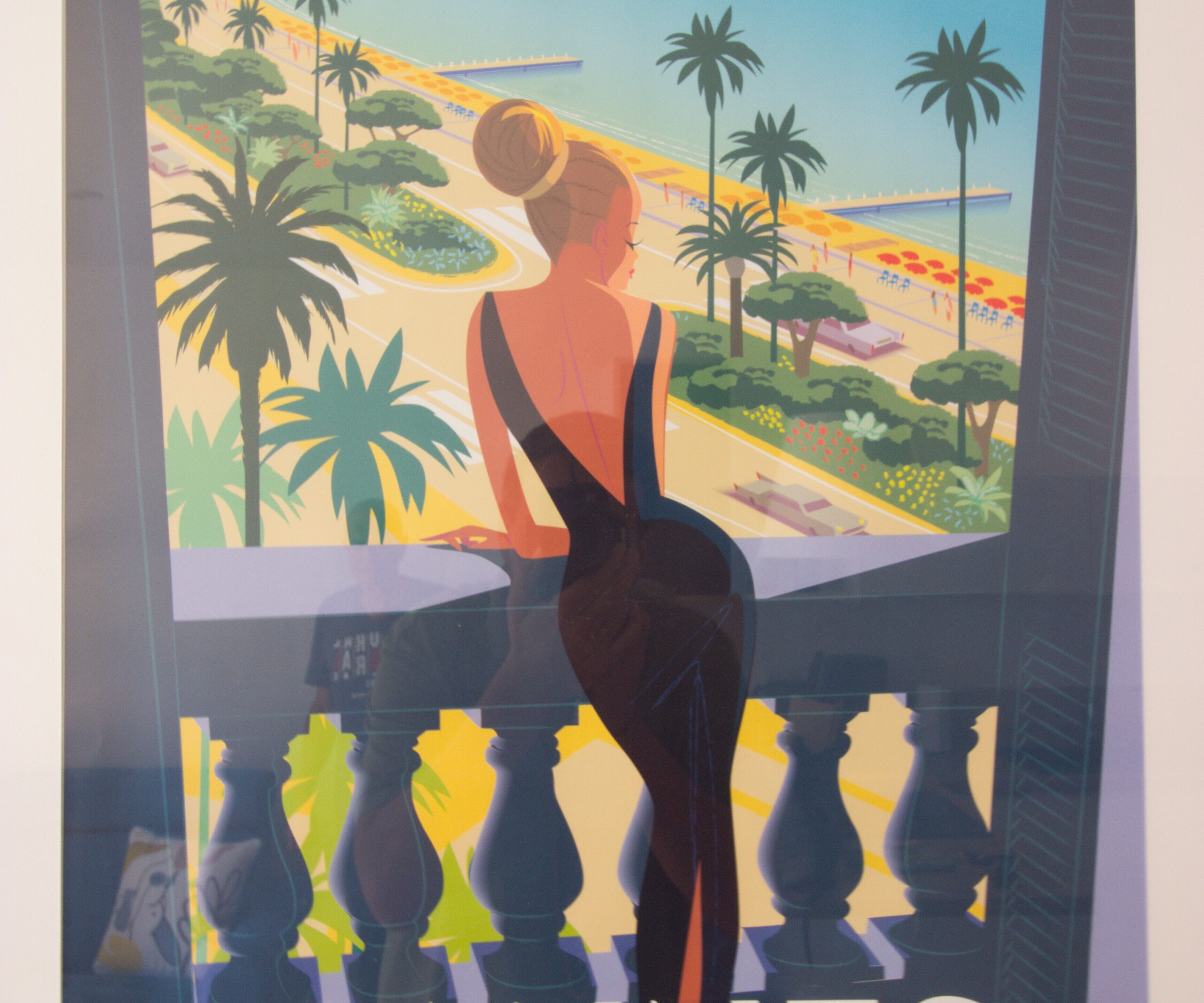 Une femme vêtue d’une robe noire est assise sur un balcon d’où l’on aperçoit des palmiers et une plage.